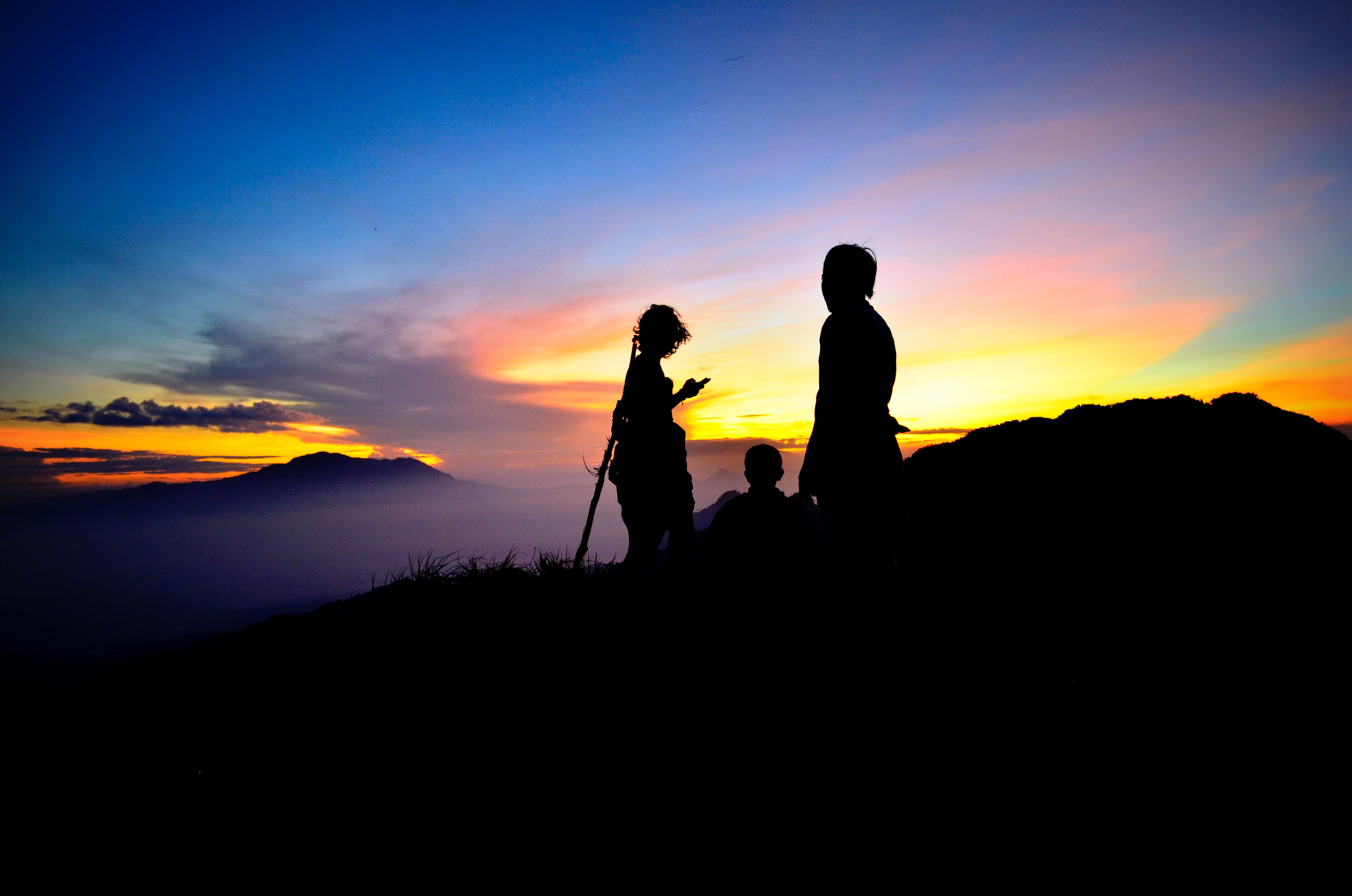 silhouette of three people on mountain with sun