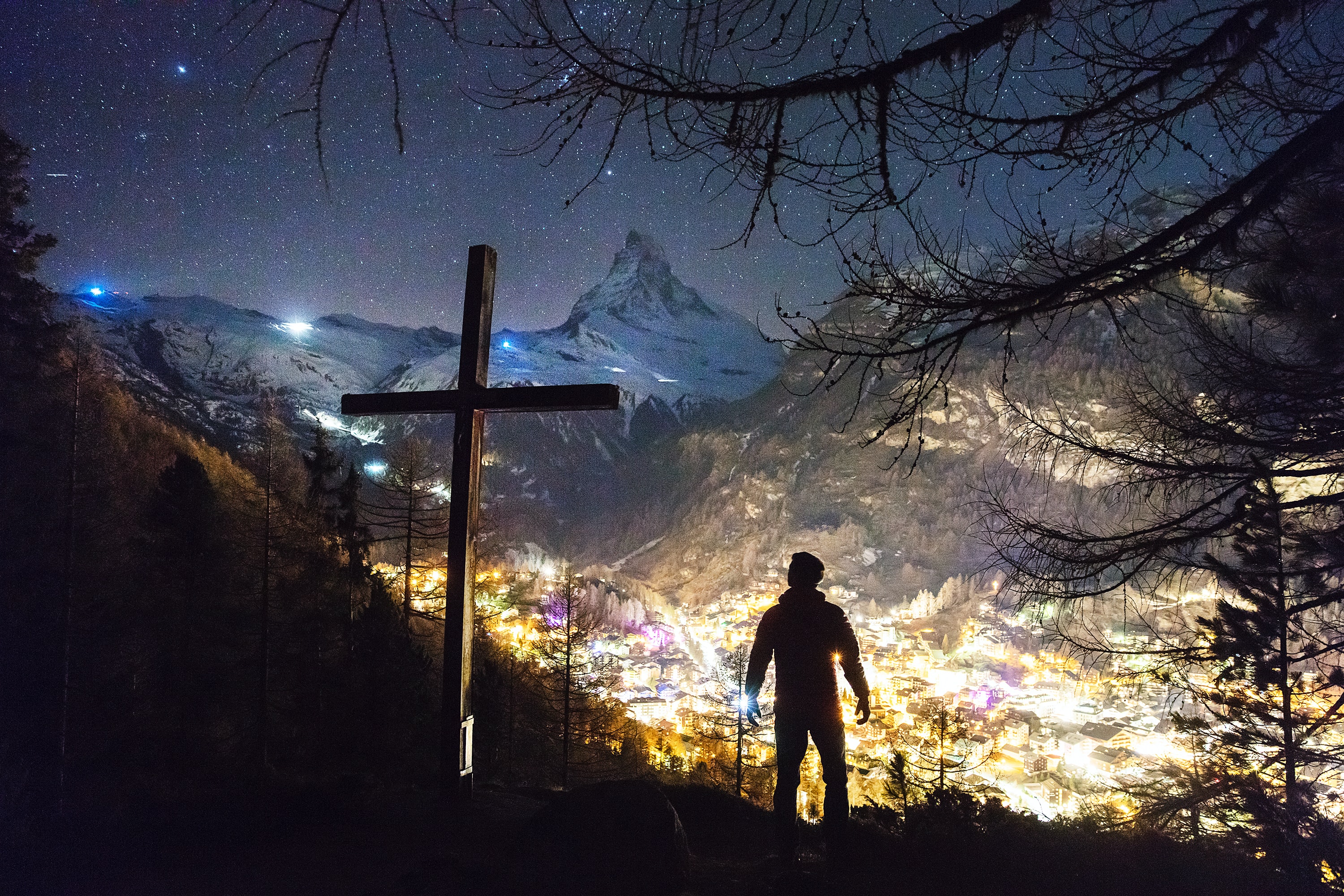 man standing near cross up mountain at night