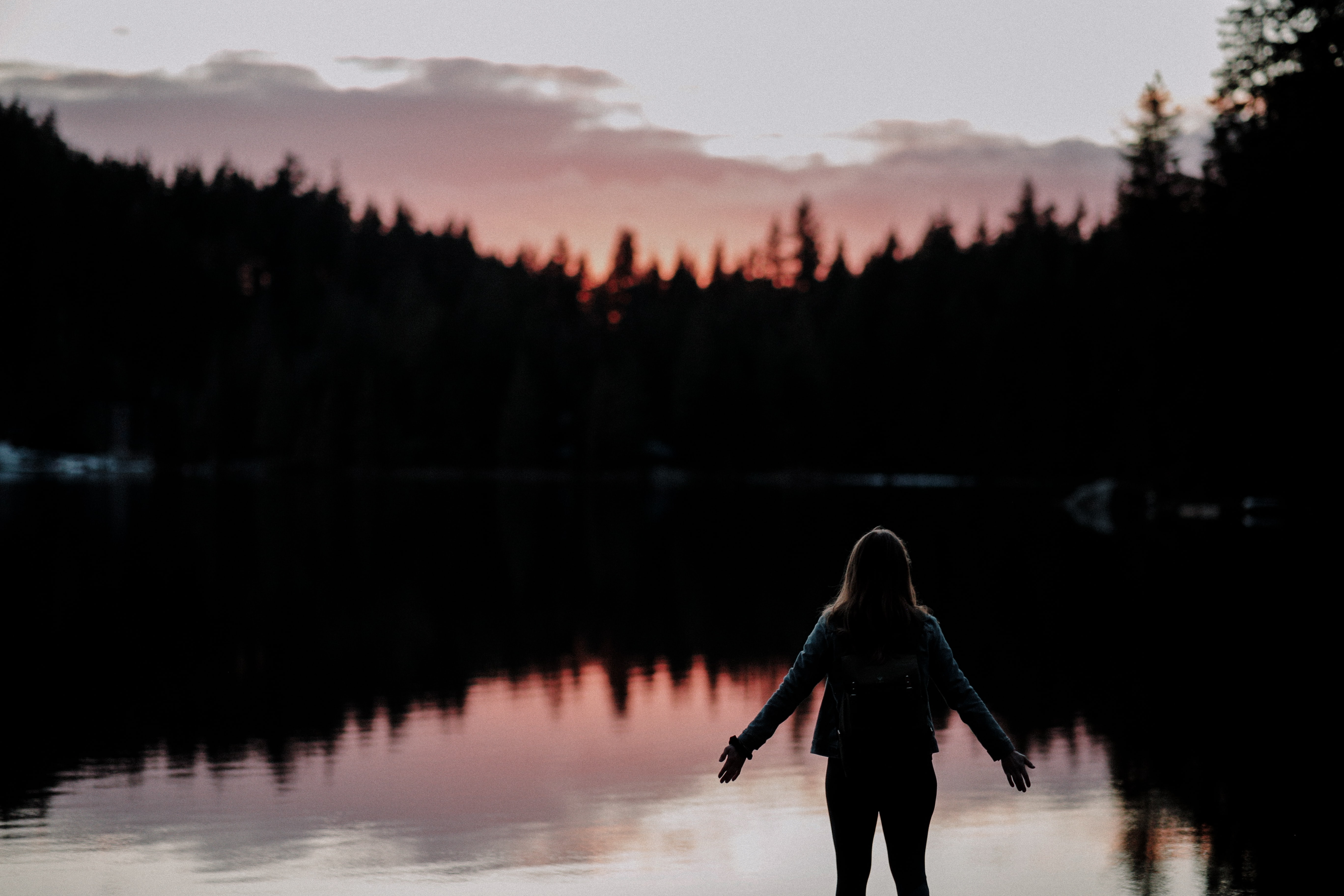 woman standing facing lake, sky, forest